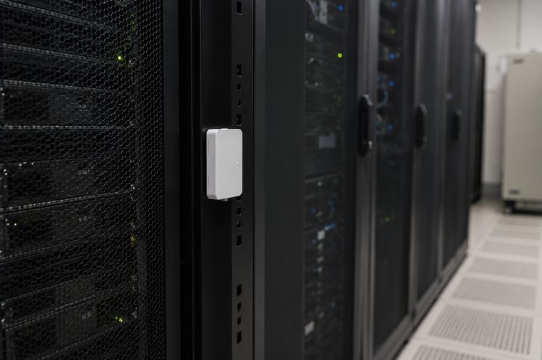 Sistem odasında server rack dikmesine monte edilmiş beyaz ısı ve nem sensörü